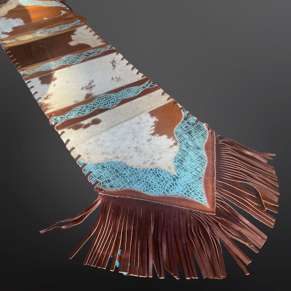 Cowhide and leather table runner with turquoise embossed leather patterns shown on a dark background.