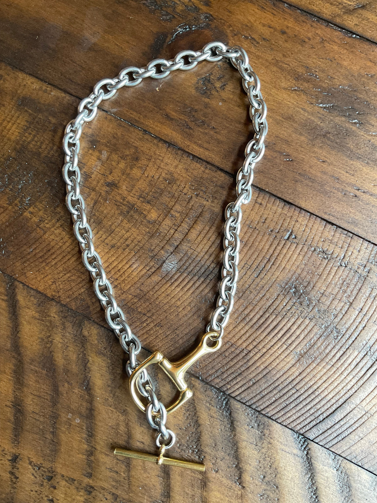 Silver chain with a gold snaffle clasp on a wooden surface