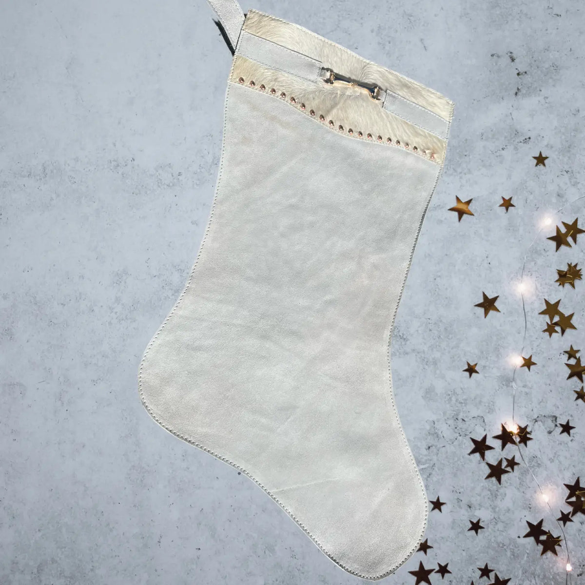 White Christmas stocking with gold trim on a textured gray background with decorative stars.