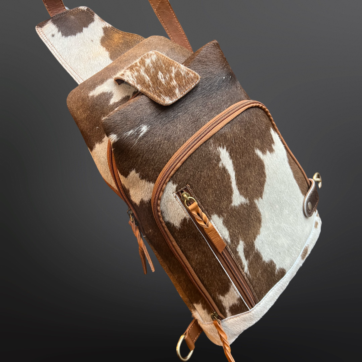 Brown and white cowhide leather bag with brown leather straps on a dark gray background