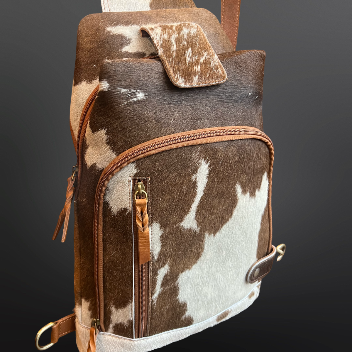 Brown and white cowhide leather bag with brown leather accents on a dark background