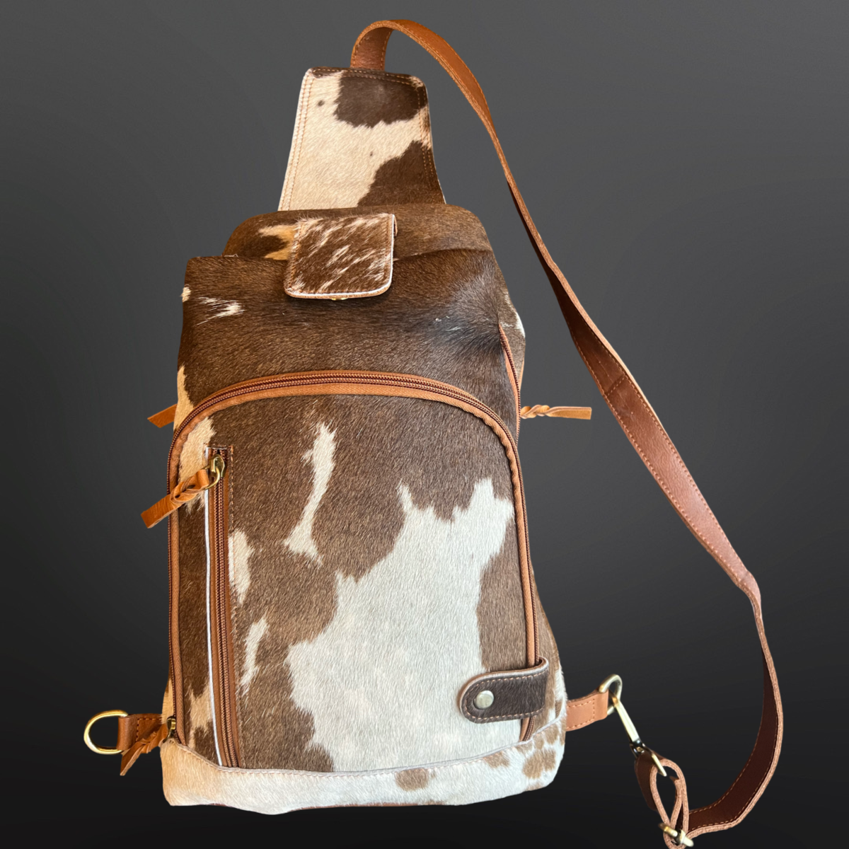 Brown and white cowhide patterned bag with a brown strap on a dark background