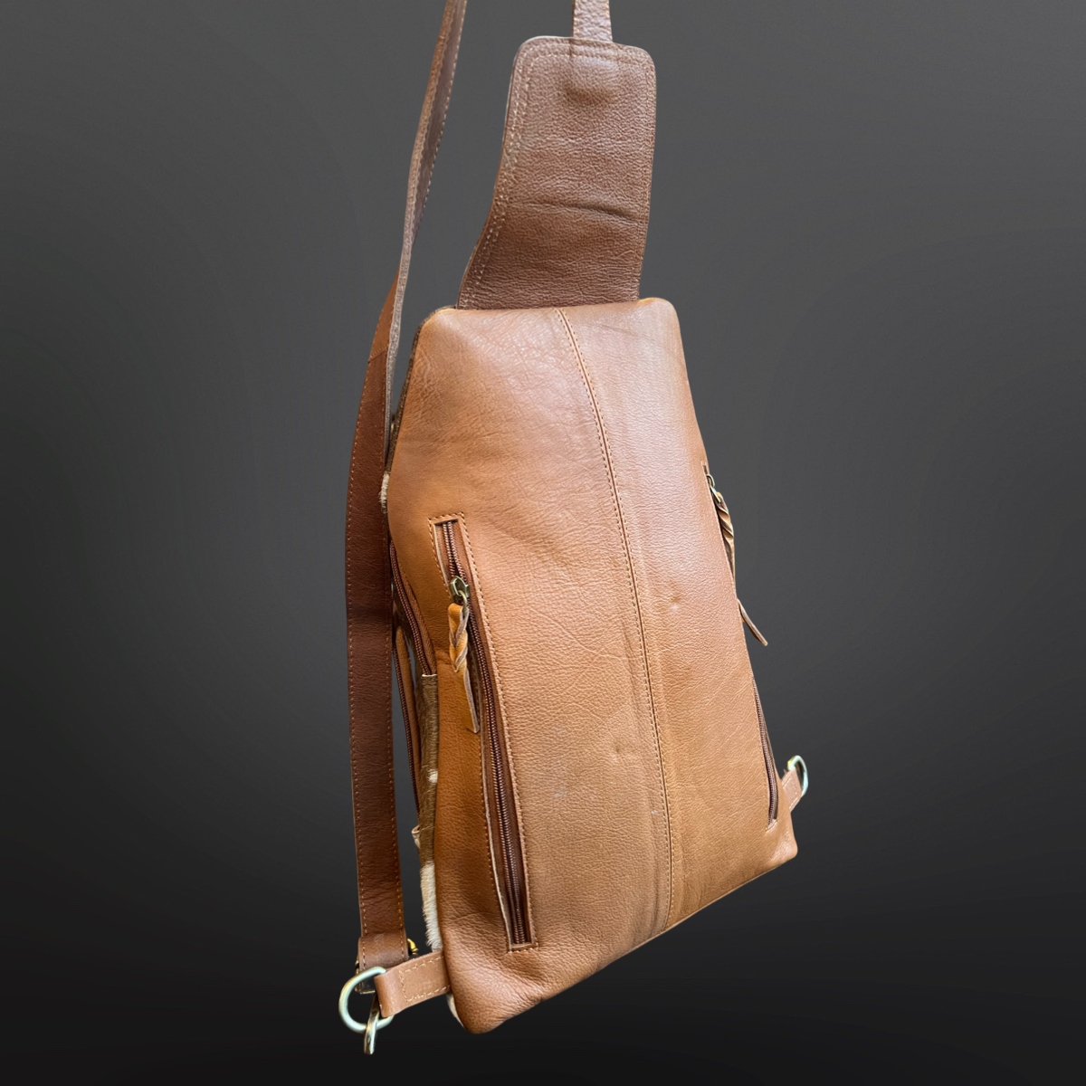 Brown leather sling bag on a dark gray background