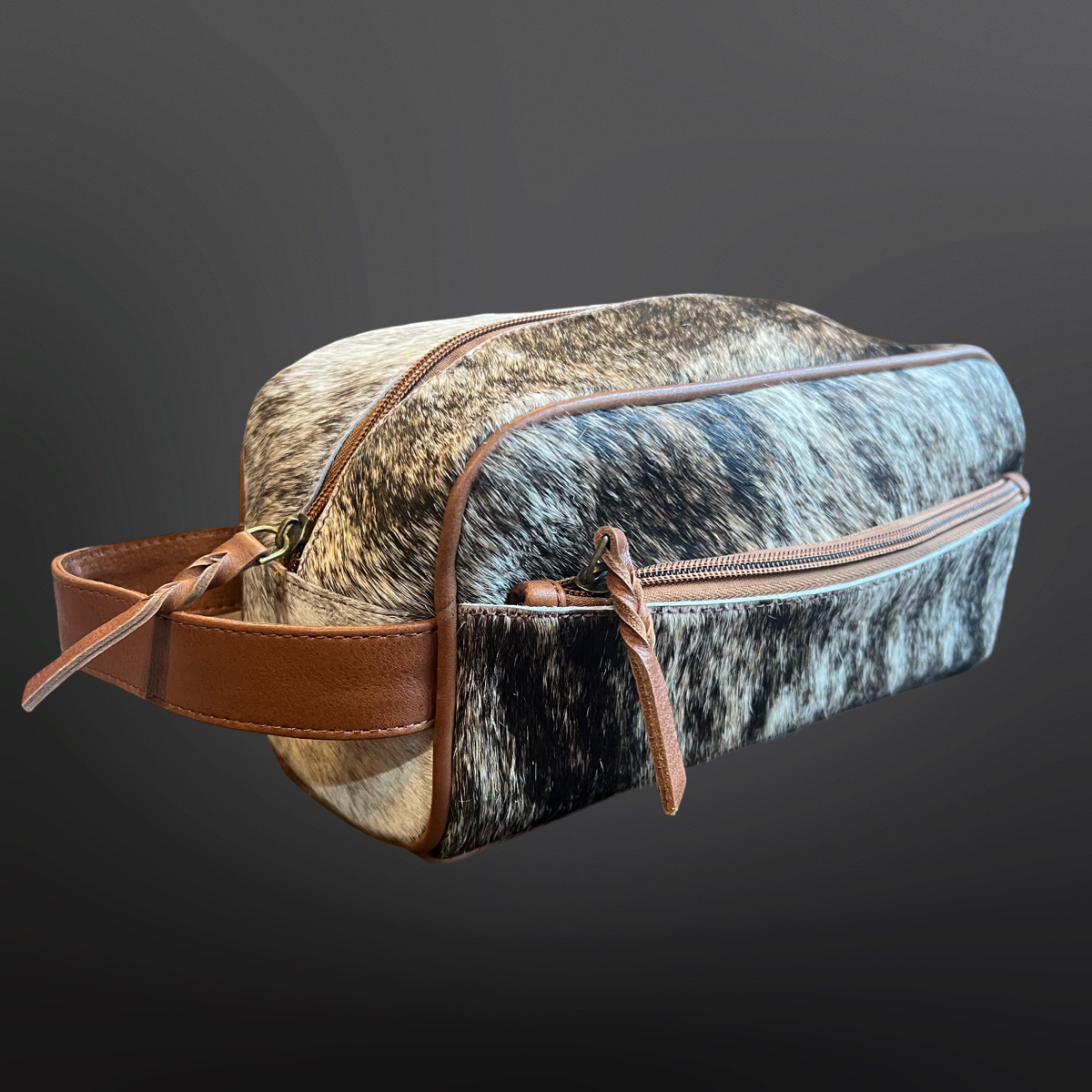 Cowhide leather toiletry bag with brown leather straps on a dark background