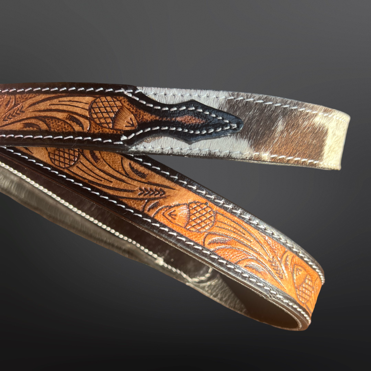 Western tooled leather and cowhide dog leash on a dark background