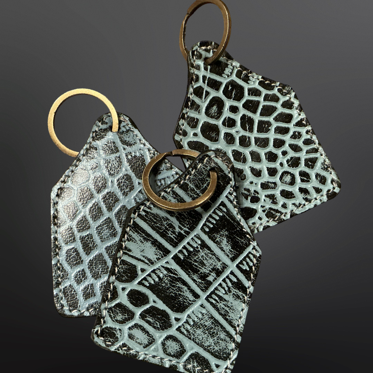 Three textured keychains with bronze rings on a dark background