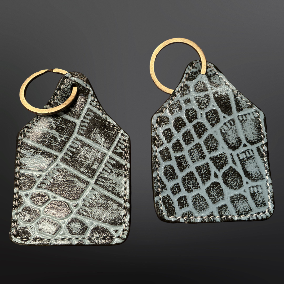 Two textured leather keychains with gold rings on a dark background