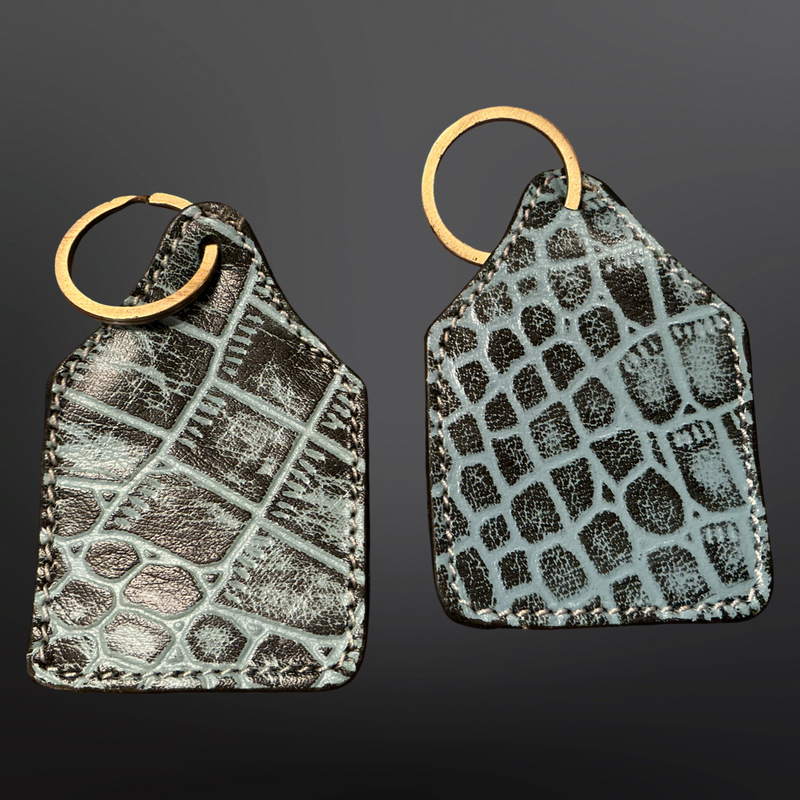 Two textured leather keychains with gold rings on a dark background