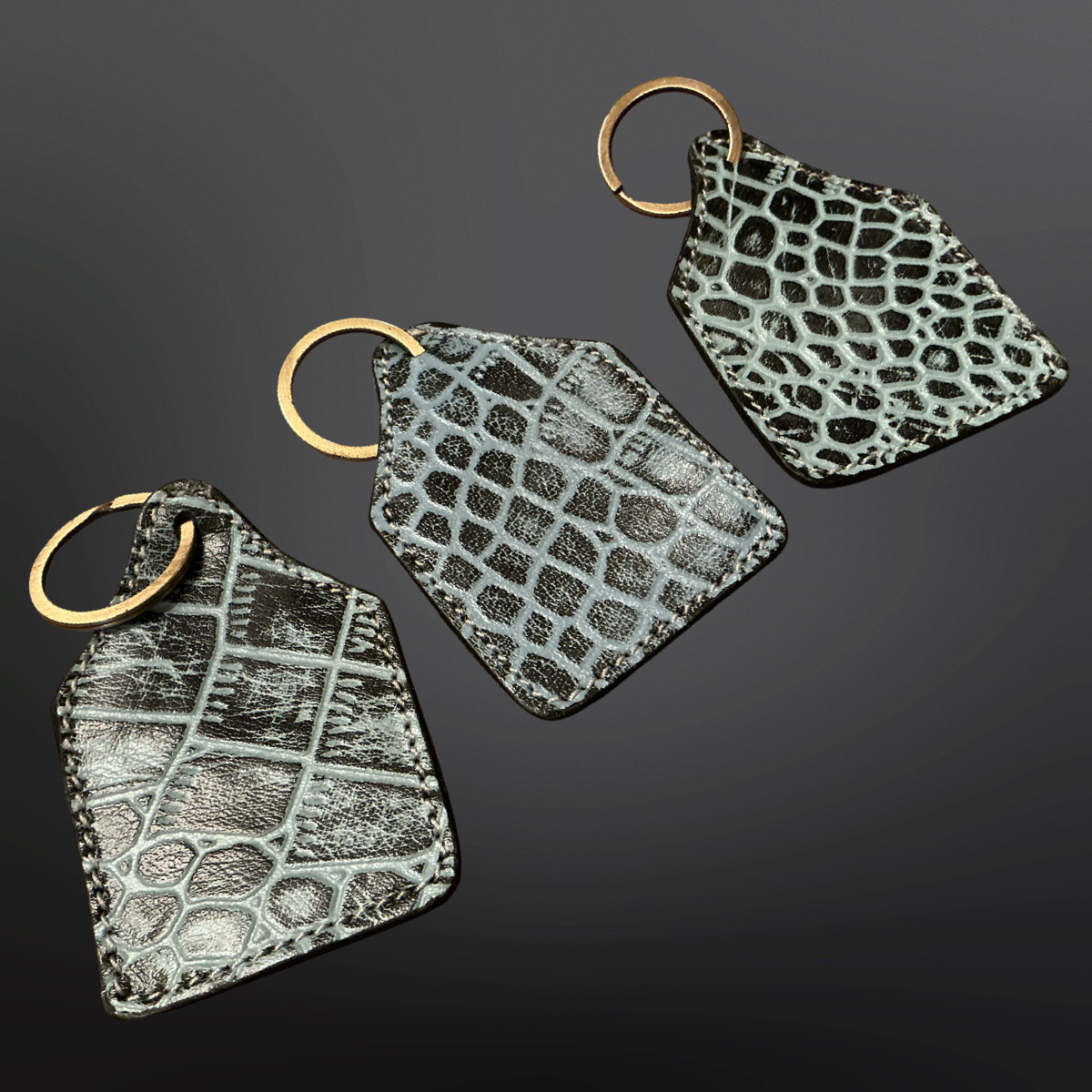 Three geometric keychains with snake skin pattern on a dark background
