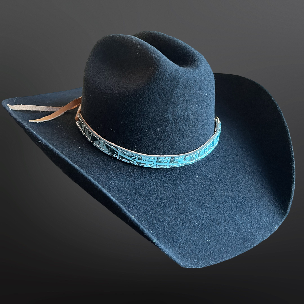Black cowboy hat with a turquoise band on a dark background