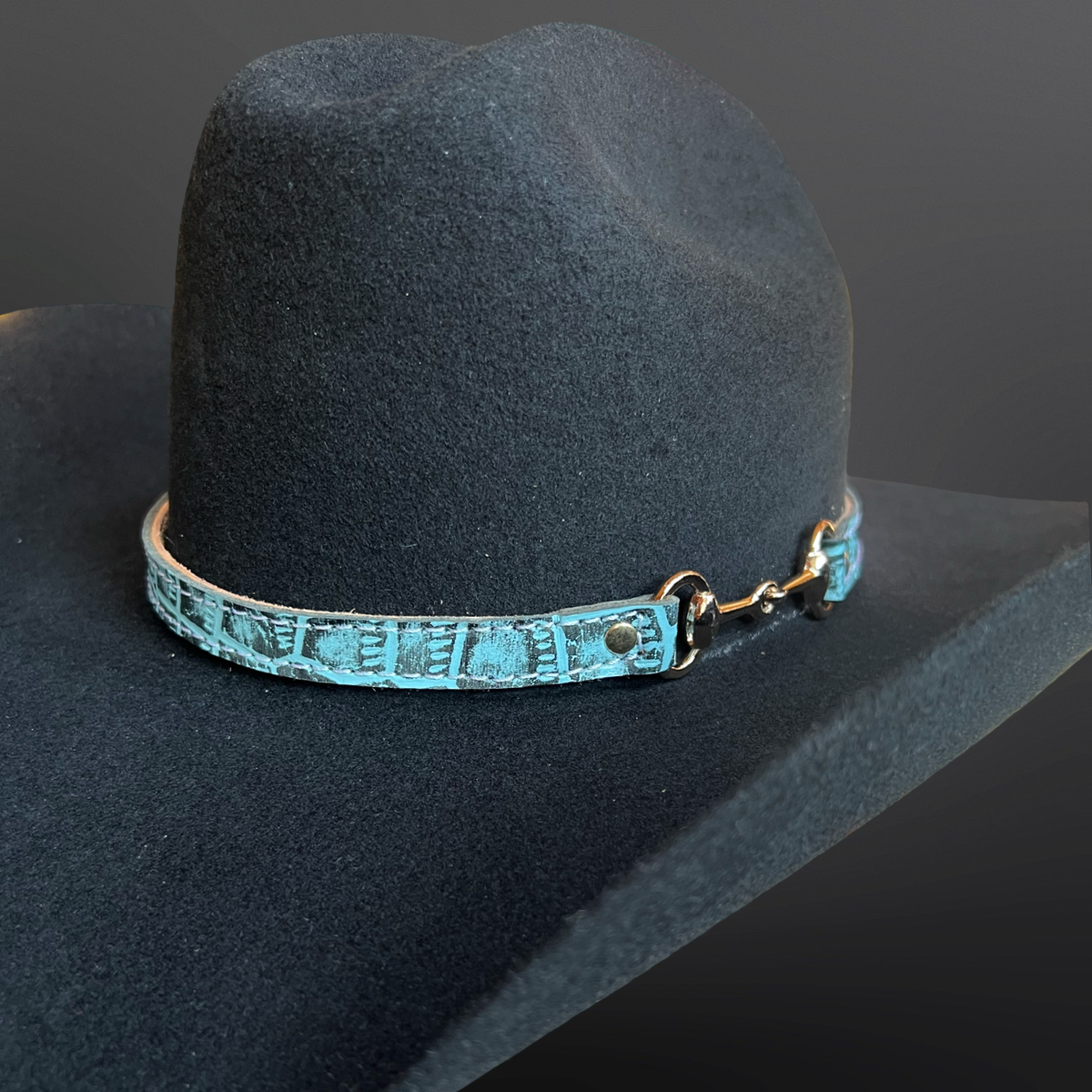 Dark gray cowboy hat with a turquoise leather band on a dark background