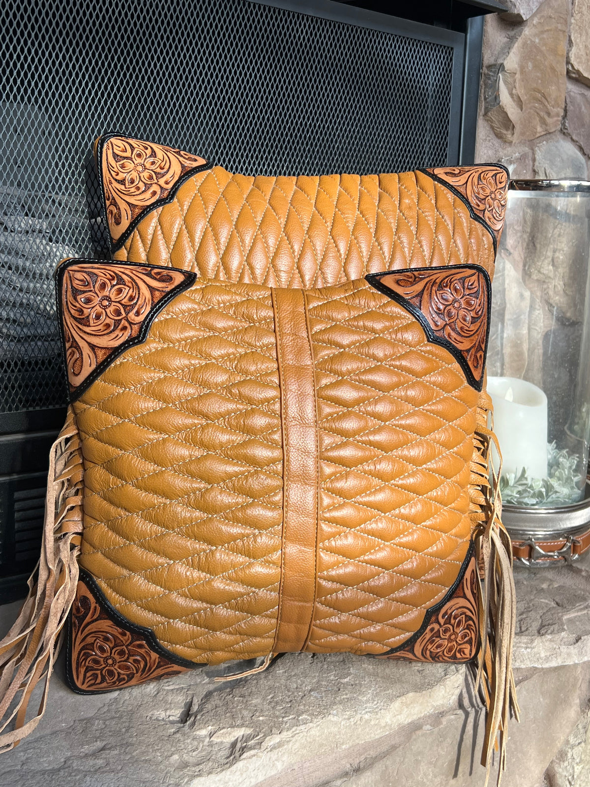 Pair of brown leather saddle pads with intricate patterns on a fireplace.