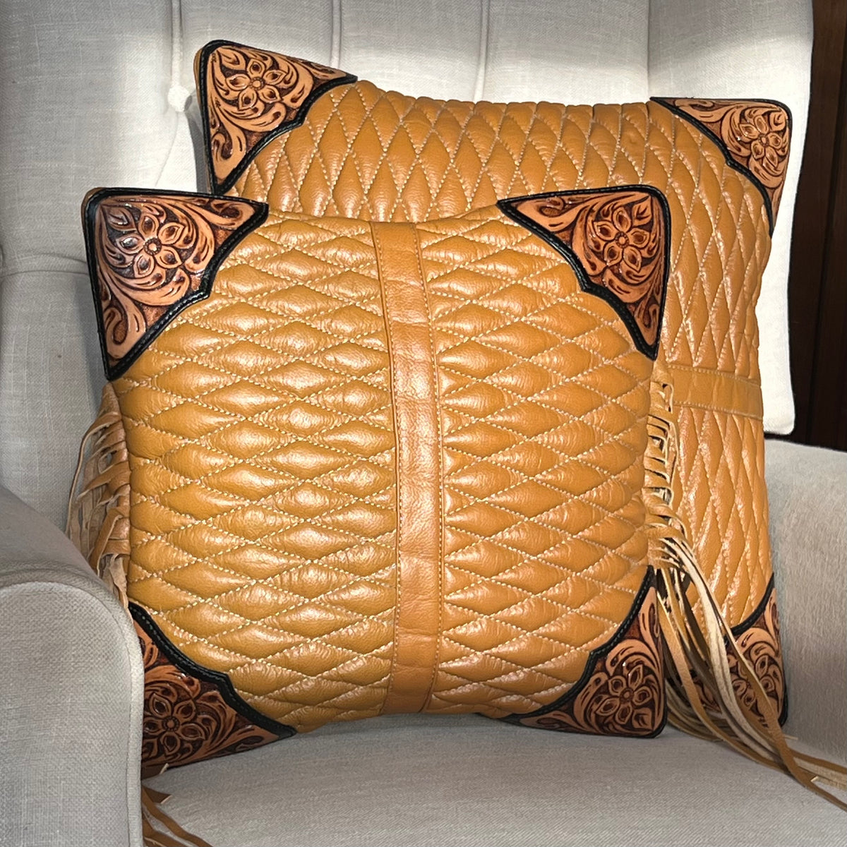Pair of quilted leather pillows with decorative corners on a gray chair.