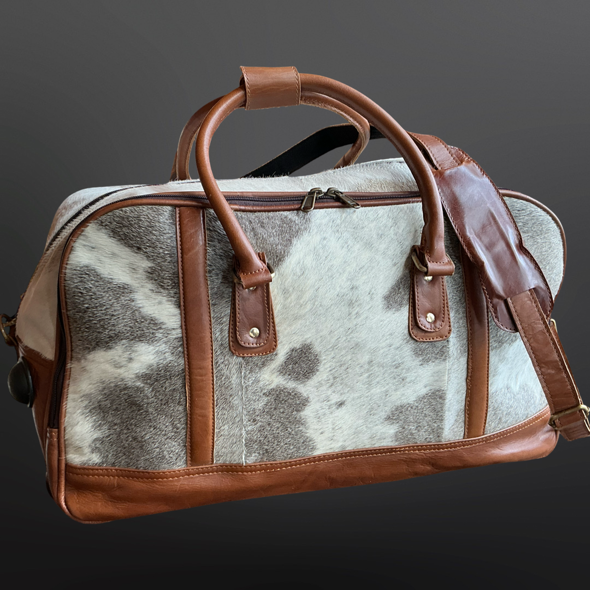 Cowhide leather duffel bag with brown leather handles and trim on a dark background