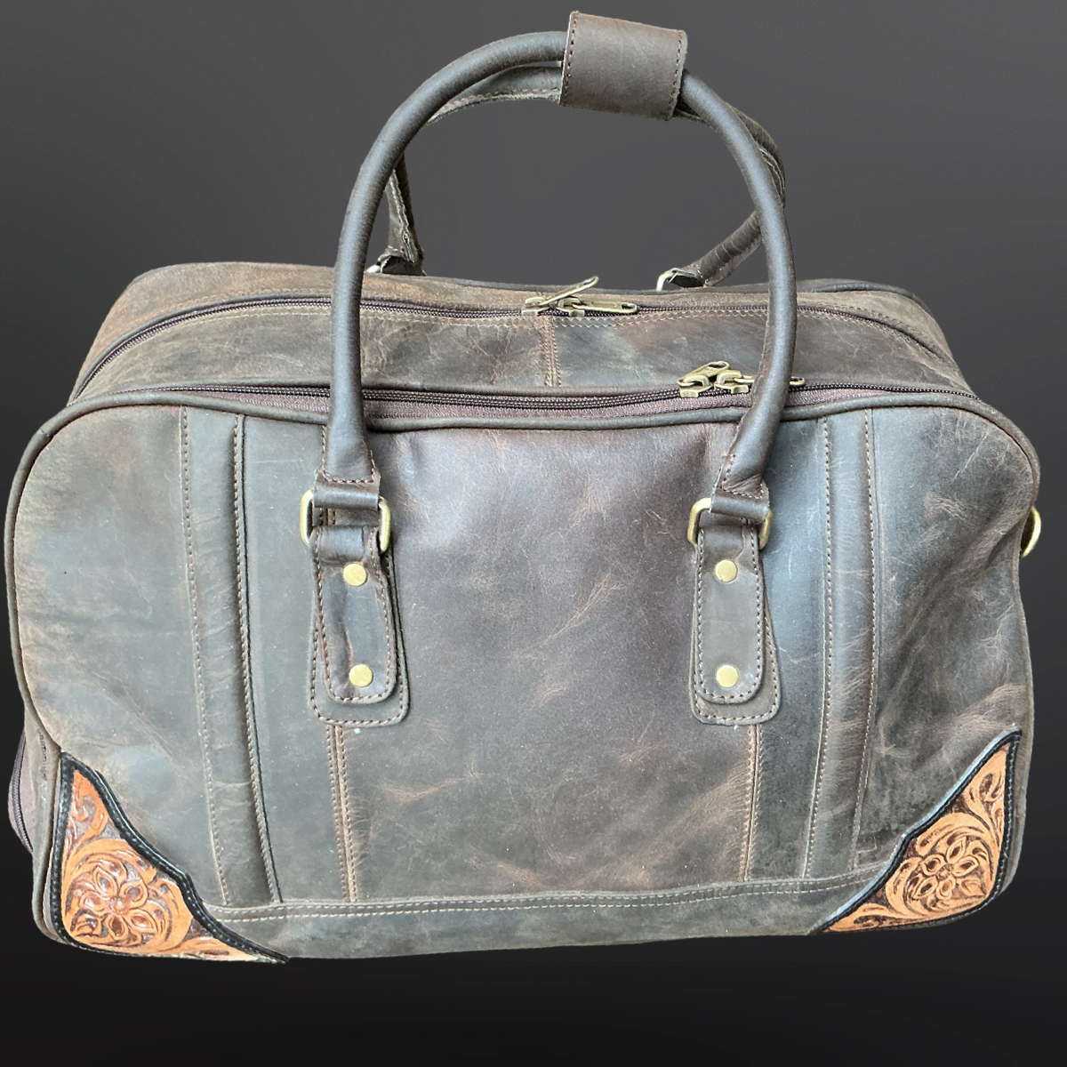 Brown leather duffel bag with decorative stitching on a dark background