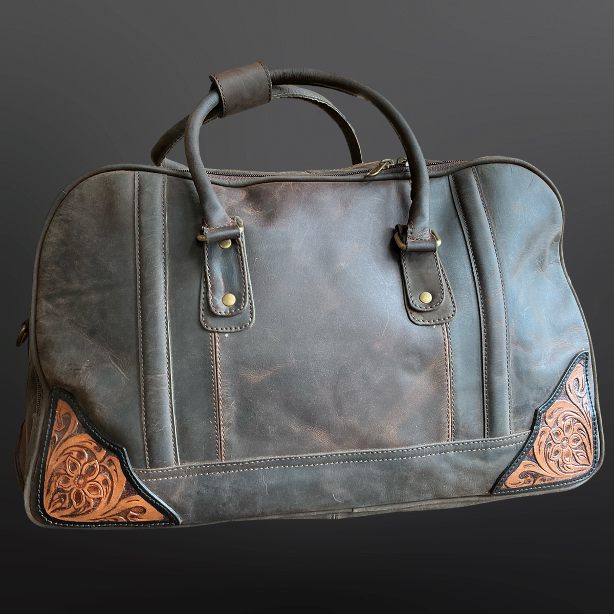 Leather duffel bag with tooled leather corners on a dark background