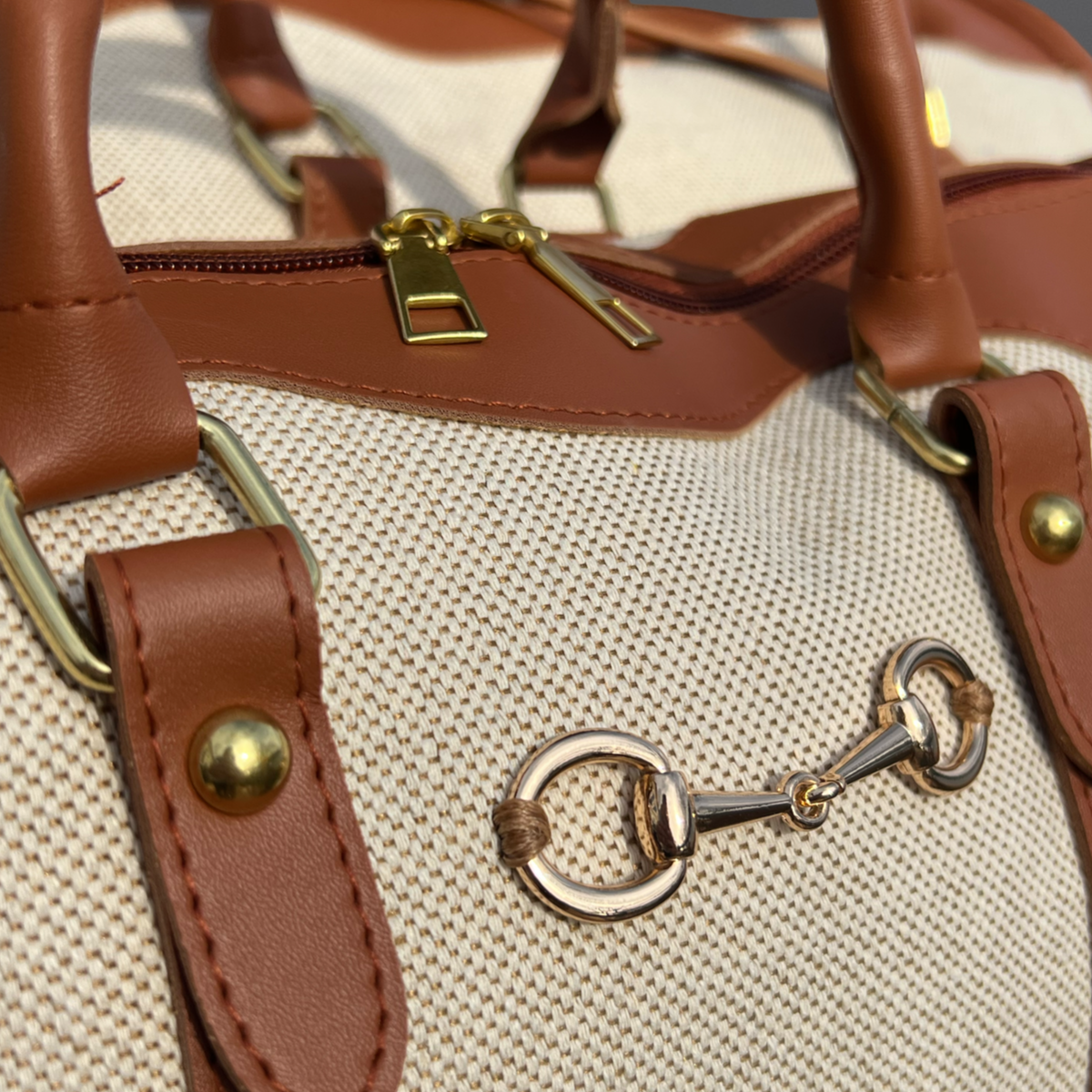 Close-up of a brown leather handbag with gold accents on a beige background