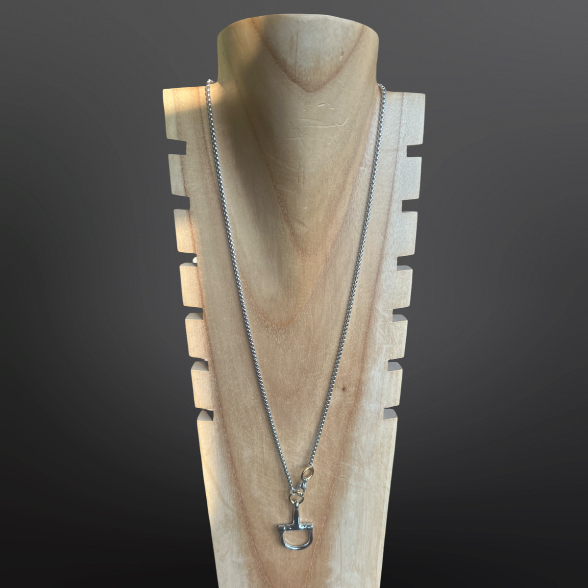 Silver necklace on a wooden mannequin against a dark background