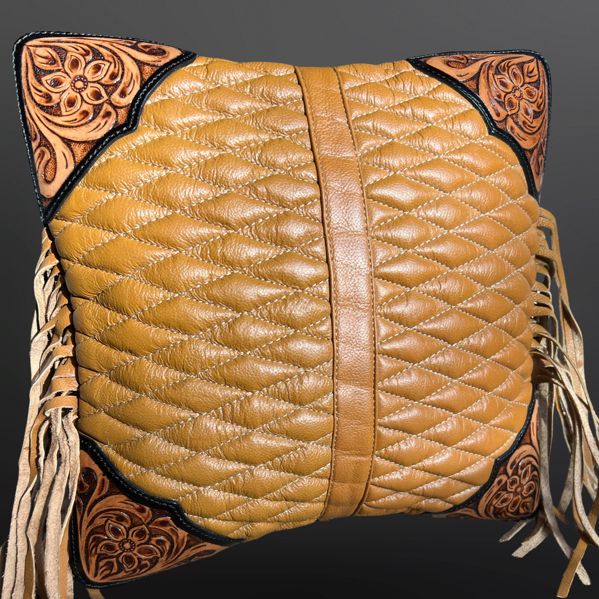 Quilted leather saddle pillow with intricate tooled leather corners on a dark background