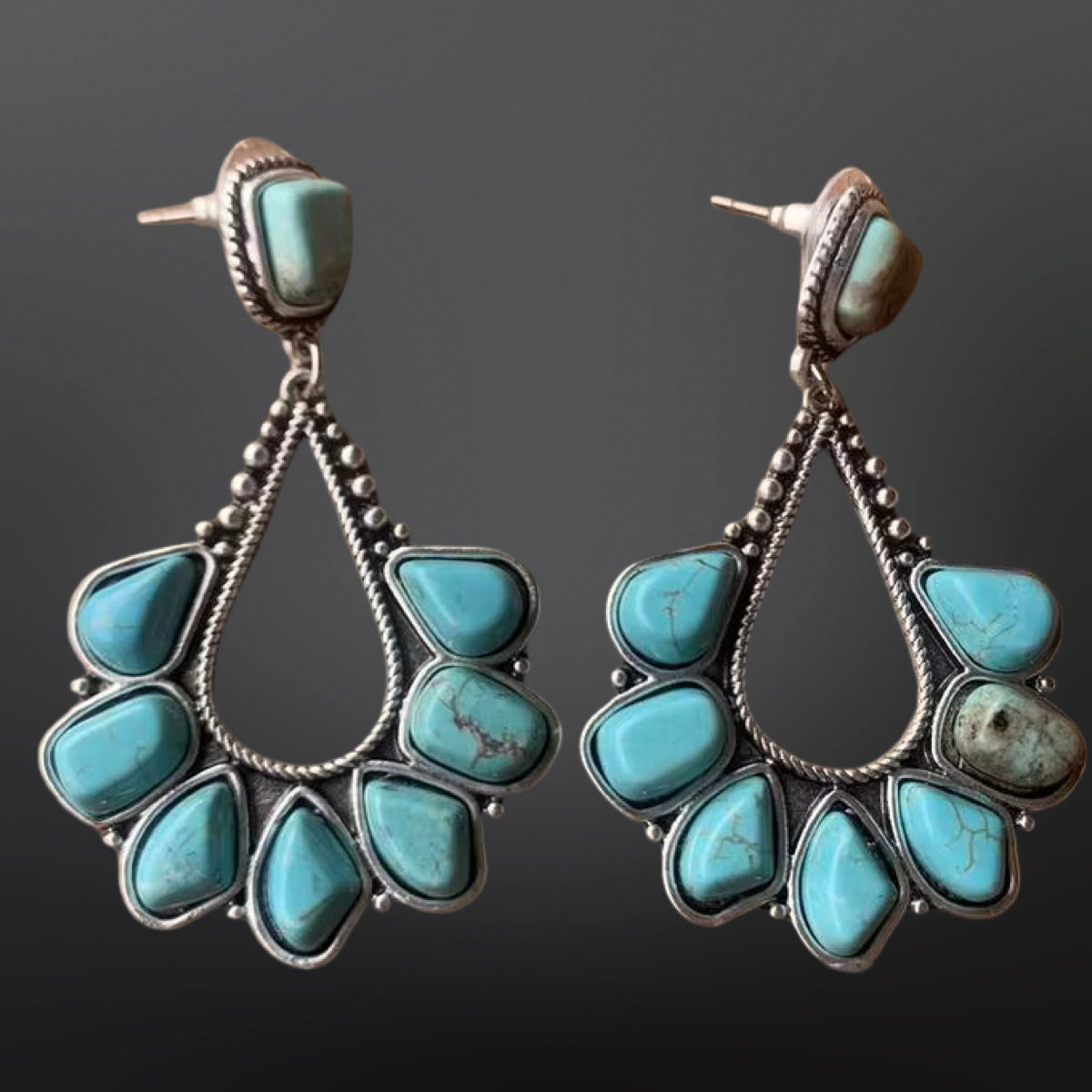 Turquoise teardrop earrings with silver accents on a dark background