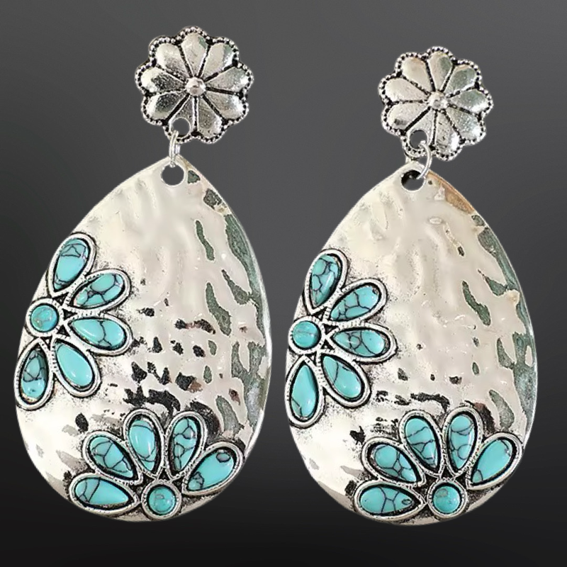 Teardrop-shaped earrings with turquoise stones and silver floral tops on a dark background