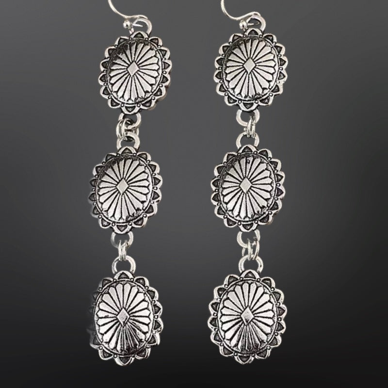 Silver concho-style earrings on a dark background